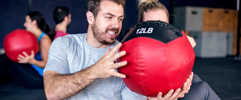 Homem e mulher a fazer exercício com bola medicinal | Holmes Place
